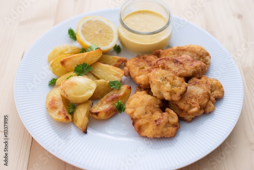 Cod fish in batter or cod fritters served with baked potatoes with parsley leaves and home made mayonnaise sauce and half of lemon served on the simple white plate. Light dish for lunch or diner. 