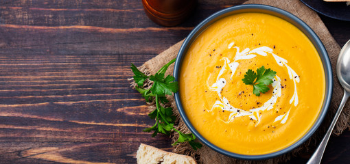 Pumpkin and carrot soup with cream and parsley on dark wooden background Top view Copy space