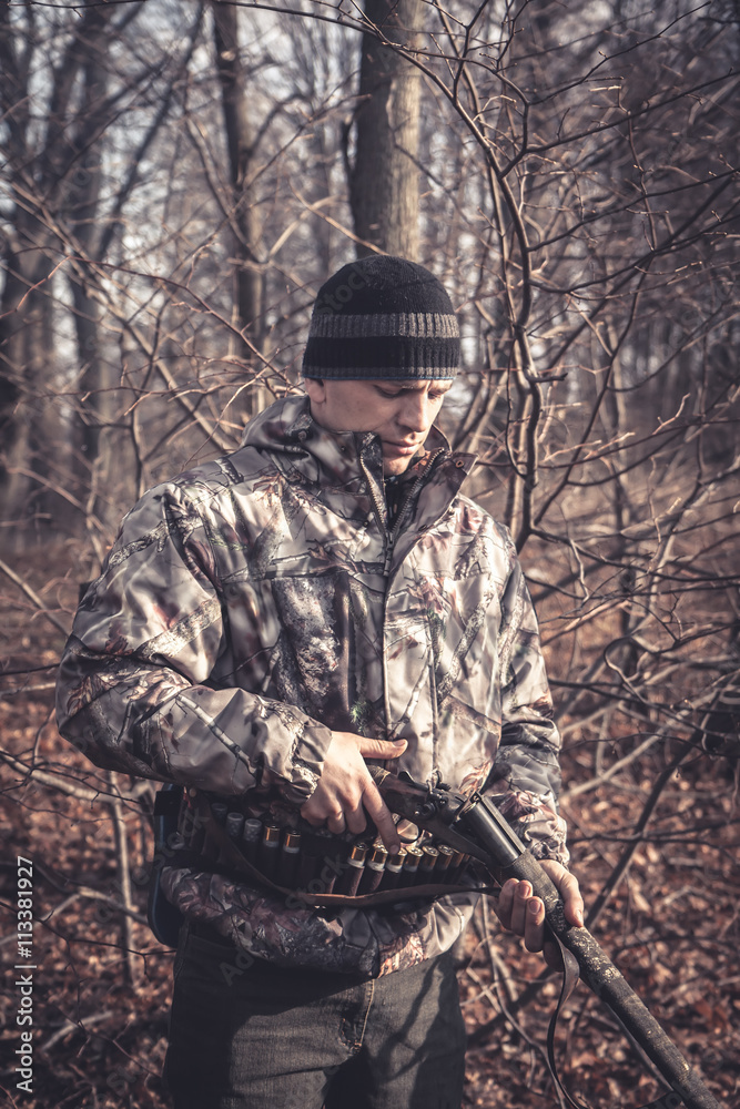Hunter man loading shotgun during hunting in autumn forest with dry trees and leaves