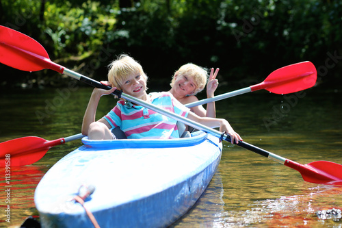 Two happy kids kayaking on the river. Active happy twin brothers, teenage school boys, having fun together enjoying adventurous experience on a sunny day during summer vacation.