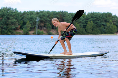 Adventurous boy learning to paddle on stand up board. Happy child, teenage schoolboy, having fun enjoying adventurous experience on the river on a sunny day during summer holidays