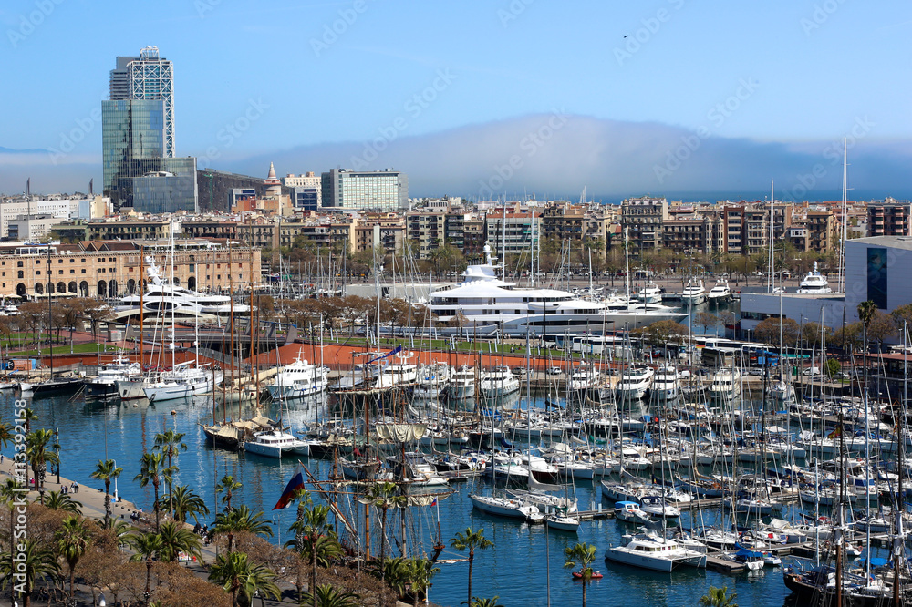 Port Vell and Barceloneta district in Barcelona, Spain. Aerial view from observation platform of Columbus monument. Private luxury yacht boats in the harbour.