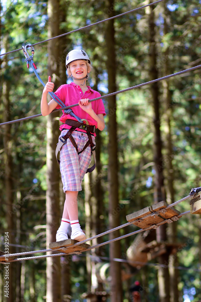 Happy teenage boy climbing on the ropes in adventure park. Healthy child enjoying outdoors teambuilding activity on a summer day.