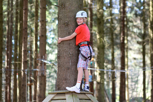 Happy teenage boy climbing on the ropes in adventure park. Healthy child enjoying outdoors teambuilding activity on a summer day.