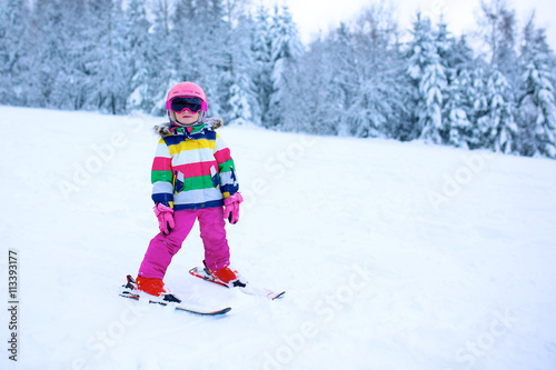 Happy child enjoying vacation in Alpine resort. Little girl skiing in mountains. Active sportive toddler wearing helmet and glasses learning to ski. Winter sport for family. Skier racing in snow.