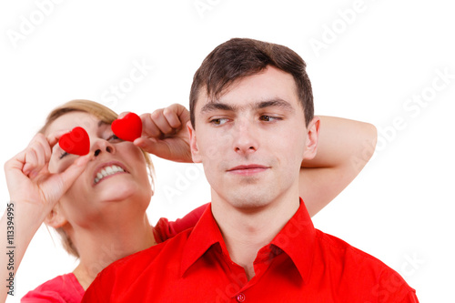 Serious man and crazy woman holds red hearts over eyes