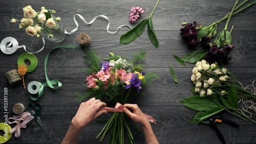 Girl's hands making bouquet of flowers over wood background. Slow motion. From above. Top view. photo
