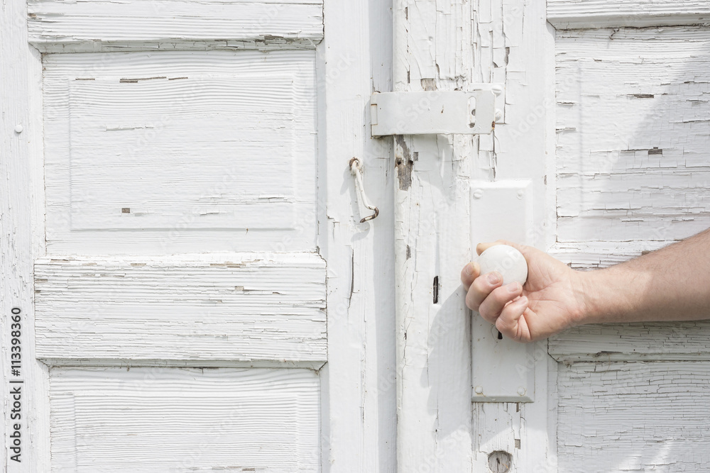 horizontal close up image of a caucasian man's hand opening a pure white rustic double door with white door knob. horizontal close up image of a caucasian man's hand opening a pure white rustic double door with white door knob.