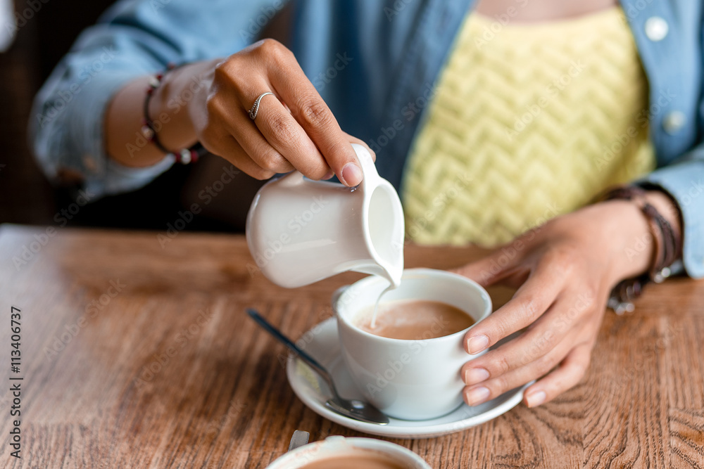 close up of woman hand pouring milk or cream to cup of coffee at close up of woman hand pouring milk or cream to cup of coffee at