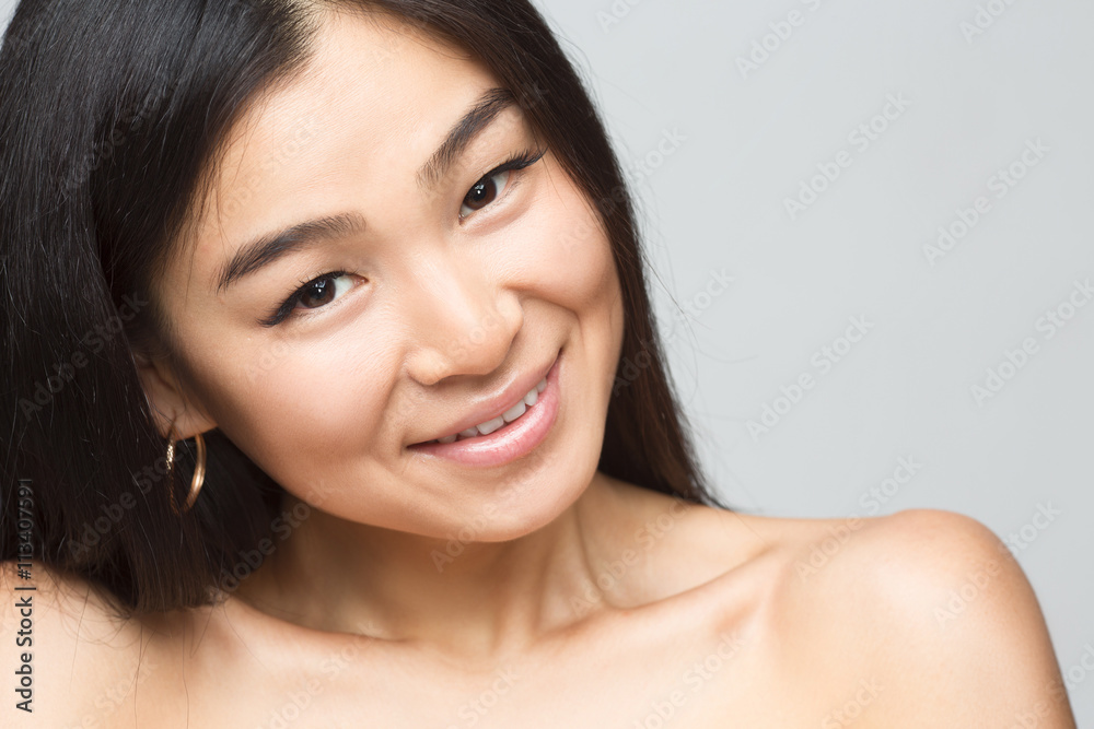 Closeup picture of cheerful asian nude lady in studio. Beautiful woman with black hair showing her beautiful shoulders isolated on grey background. Closeup picture of cheerful asian nude lady in studio. Beautiful woman with black hair showing her beautiful shoulders isolated on grey background.
