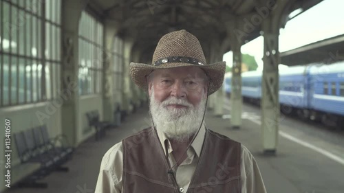 Portrait of senior man in greeting takes off his hat on train station with train on the background