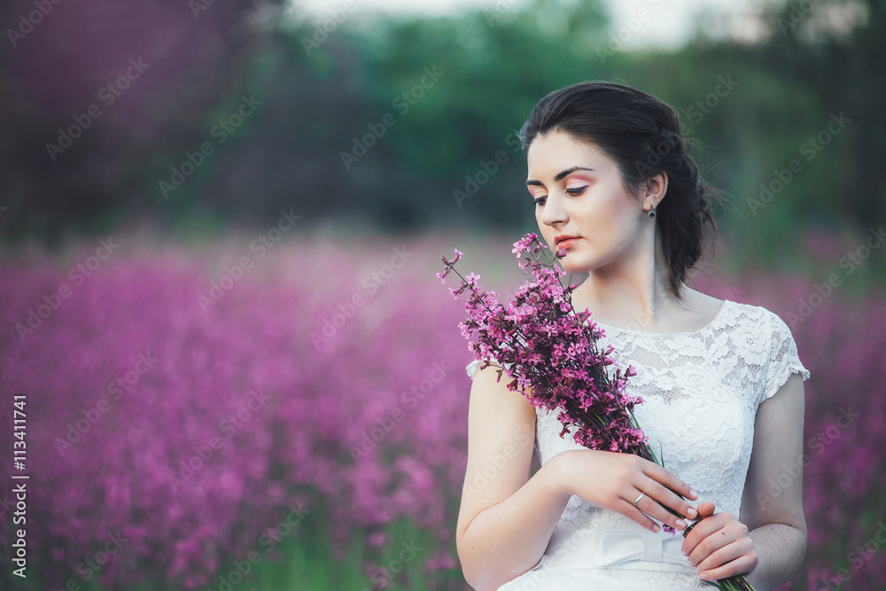 beautiful bride in a flower field. The girl in a white dress with a bouquet in a summer field at sunset beautiful bride in a flower field. The girl in a white dress with a bouquet in a summer field at sunset