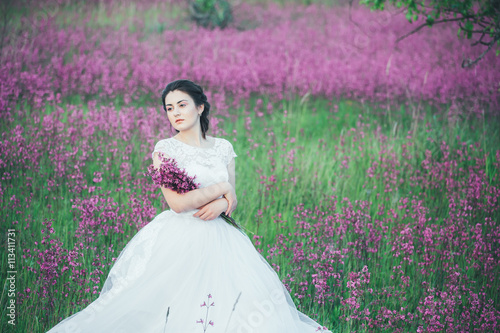 beautiful bride in a flower field. The girl in a white dress with a bouquet in a summer field at sunset