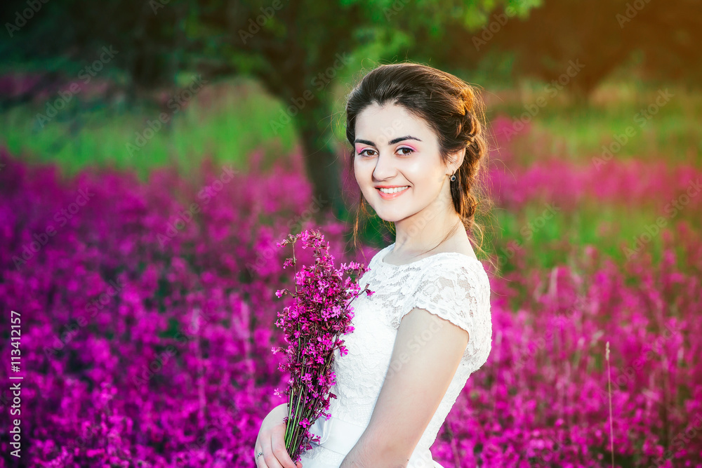 beautiful bride in a flower field. The girl in a white dress with a bouquet in a summer field at sunset beautiful bride in a flower field. The girl in a white dress with a bouquet in a summer field at sunset
