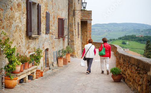 Two senior woman walking along street in medieval city Pienza in Tuscany, Italy. © Feel good studio