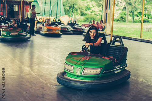 Cute young woman having fun in electric bumper car in amusement park