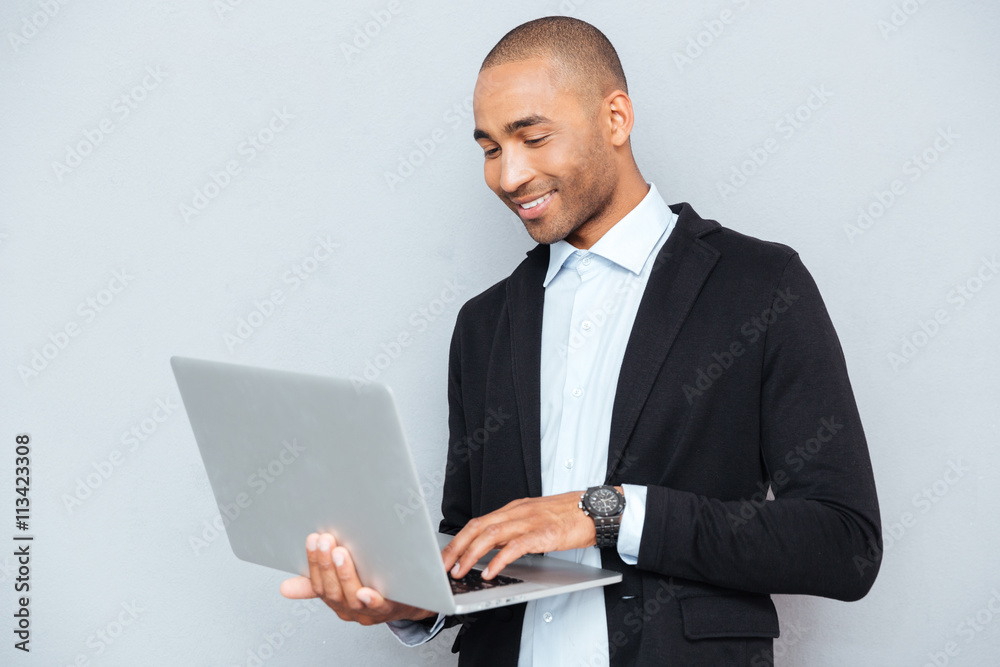 Smiling african american young man standing and using laptop Smiling african american young man standing and using laptop
