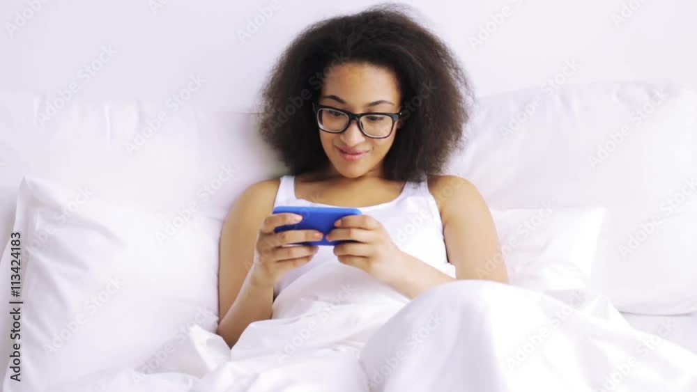 african woman with smartphone in bed at home african woman with smartphone in bed at home