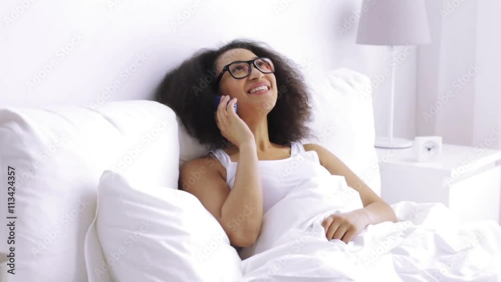 african woman calling on smartphone in bed at home african woman calling on smartphone in bed at home