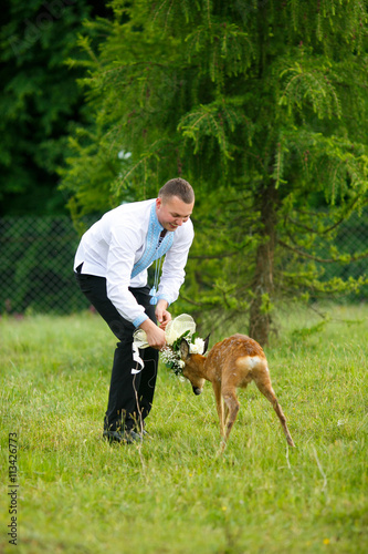 Little deer attacks a wedding bouqet held by a groom in embroide photo
