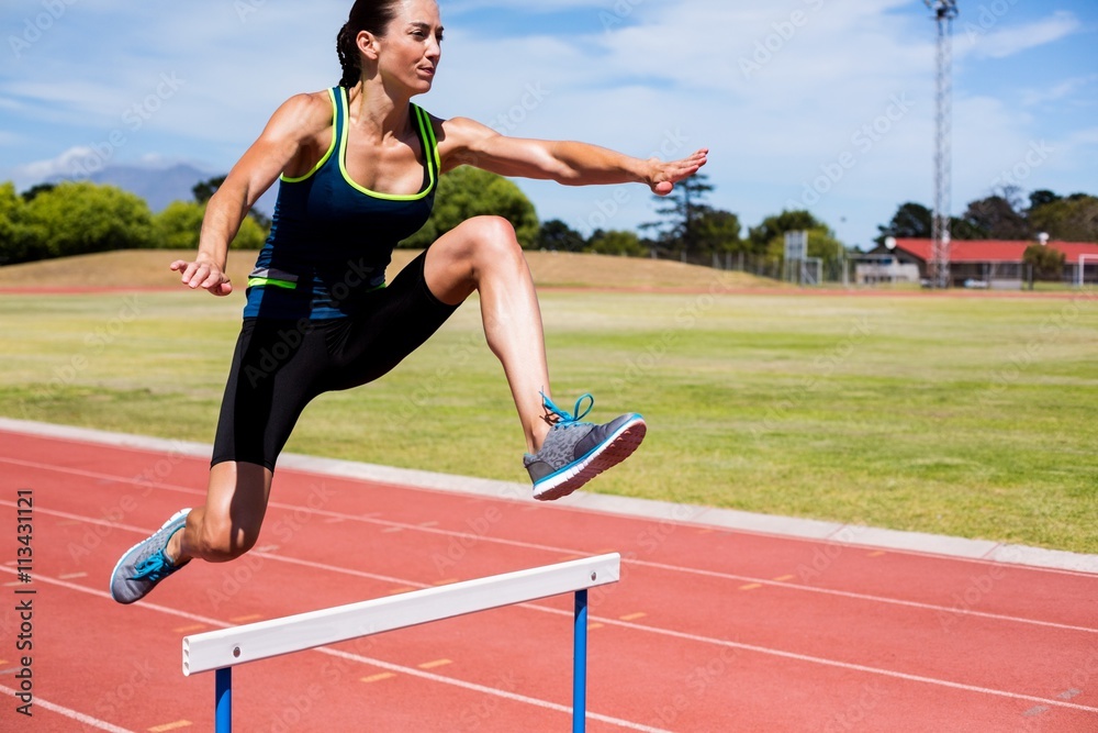 Obraz premium Female athlete jumping above the hurdle