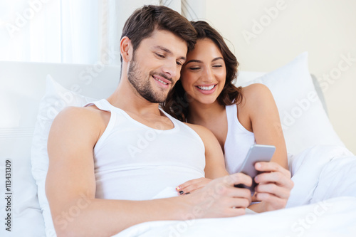 Young sweet couple in bed looking at a mobile phone