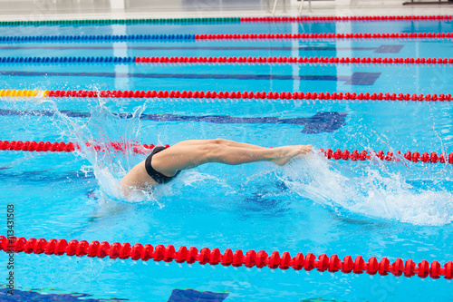 Young muscular swimmer jumping from starting block in a swimming pool