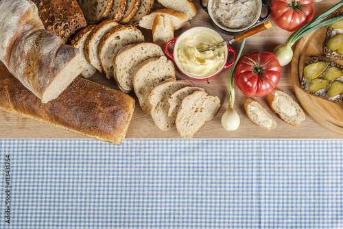 Stół zastawiony chlebem, pomidorami, cebulkami i smalcem na śniadanie na stole z obrusem w kratę photo