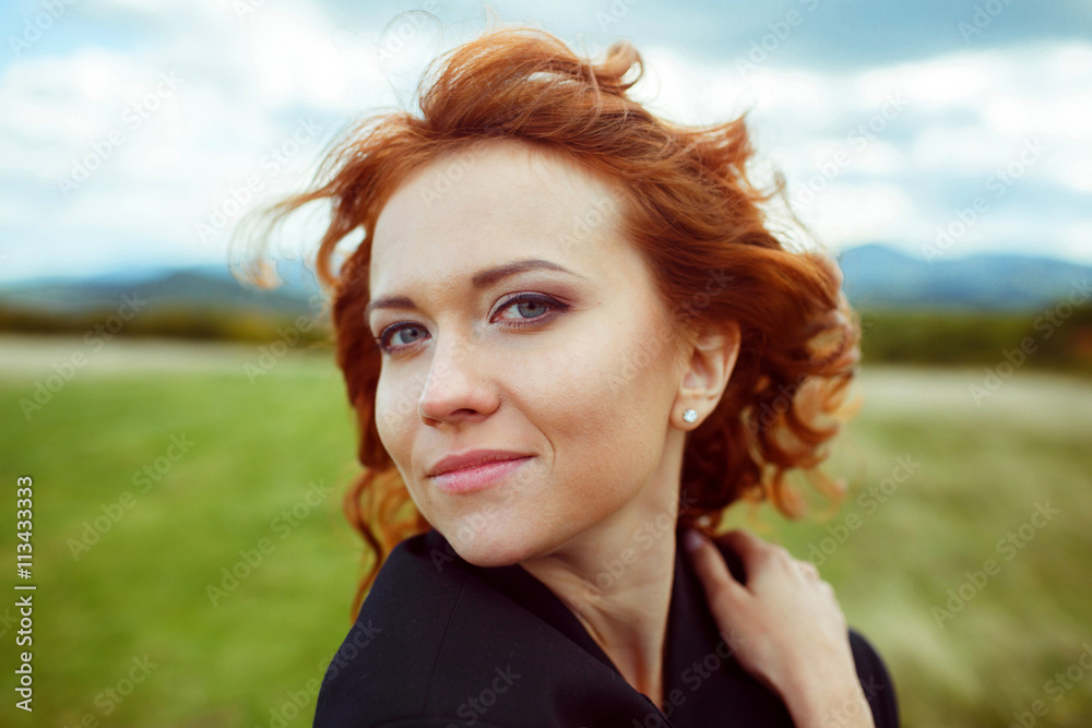 Fototapeta premium Lady with red curly hair looks stunning while wind blows along h