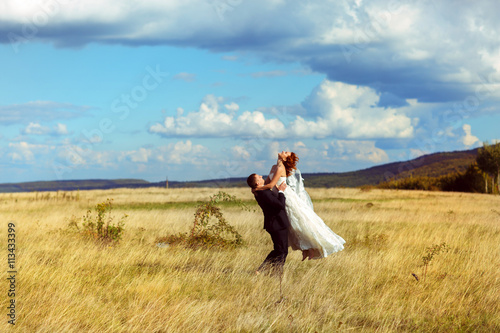 Groom rises bride up standing on the field under a deep blue sky © IVASHstudio