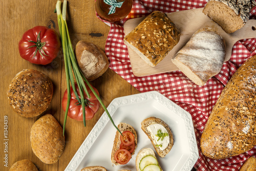 Pełnoziarnisty chleb, pomidory, szczypiorek i gotowe kanapki na drewnianym stole