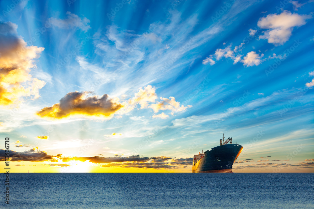 Cargo ship sailing on sea at sunset.