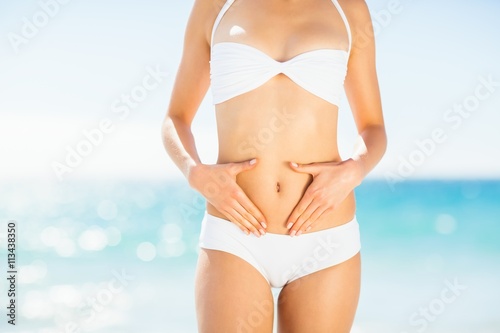 Mid section of woman in bikini touching her belly