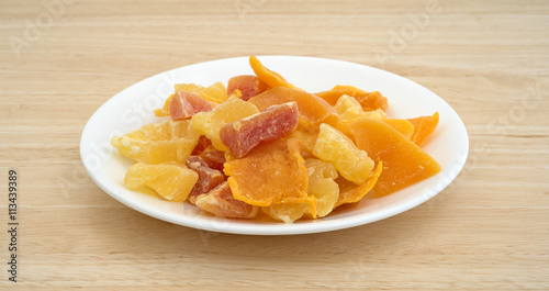 Plate of sugared pineapple, mango and papaya on a wood table top side view.