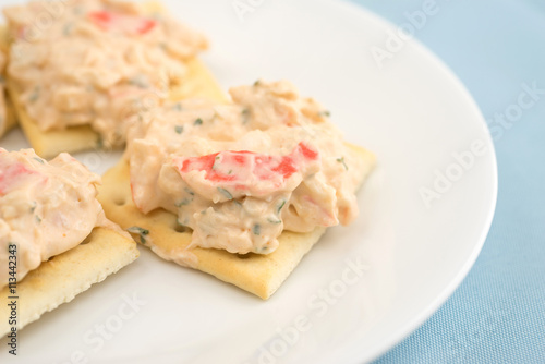 Lobster dip on saltine crackers on blue table cloth side view.