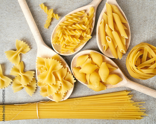 Various types of pasta on grey background, from above