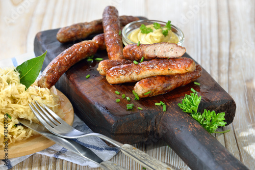Foto Nürnberger Rostbratwürste mit Senf auf einem rustikalen Steakbrett mit Sauerkrau