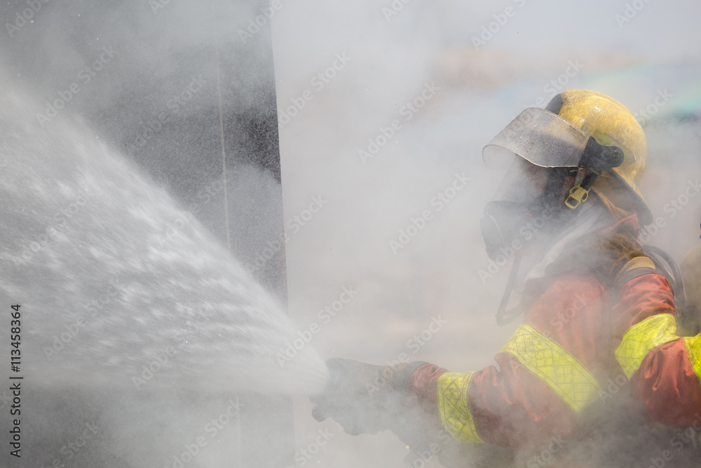 Fototapeta premium fireman in fire fighting suit spraying under smoke and drizzle