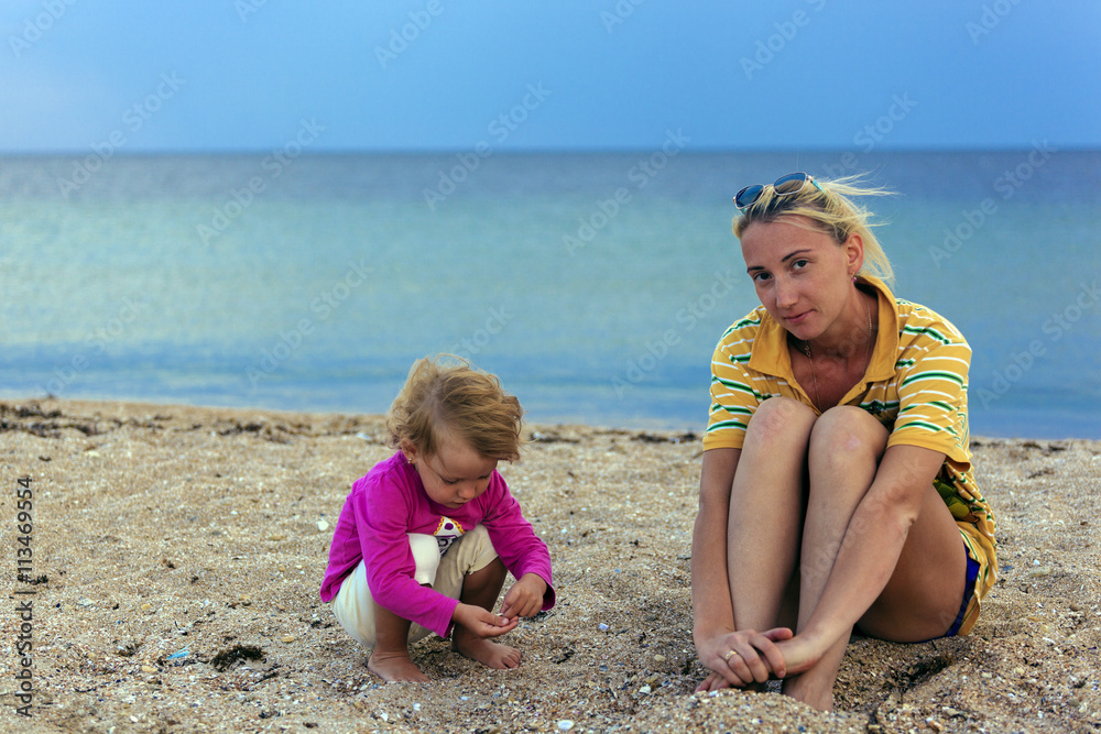 Mother and daughter sitting on the sand after sunset