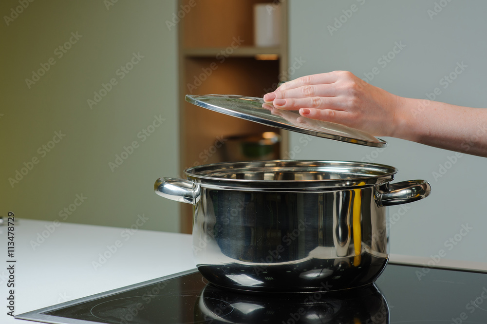 Female hand holding the lid of the pan. Person removing lid from