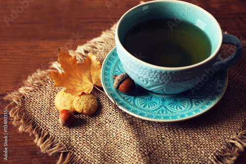 Cup of tea with autumn decor on wooden table.