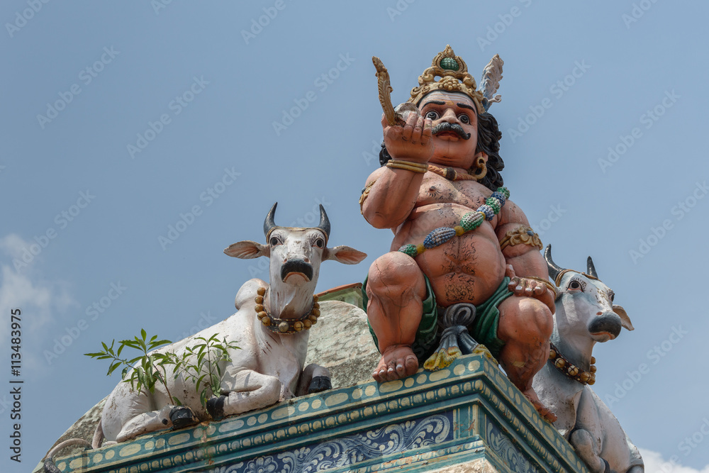 Chettinad, India - October 17, 2013: Detail of the Shiva temple at Kottaiyur shows half-naked Ayyanar on wall in company of two bulls against blue sky.