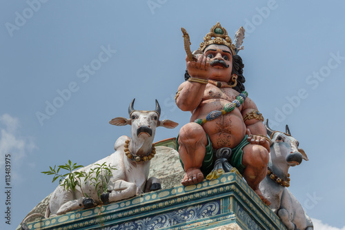 Chettinad, India - October 17, 2013: Detail of the Shiva temple at Kottaiyur shows half-naked Ayyanar on wall in company of two bulls against blue sky. © Klodien