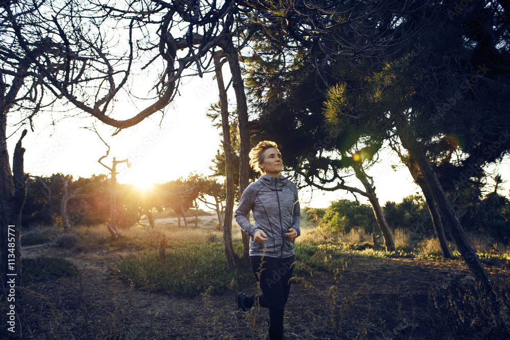Woman jogging on field by trees during sunrise Woman jogging on field by trees during sunrise