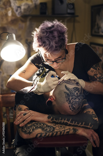 Woman tattoo artist tattooing male client in studio