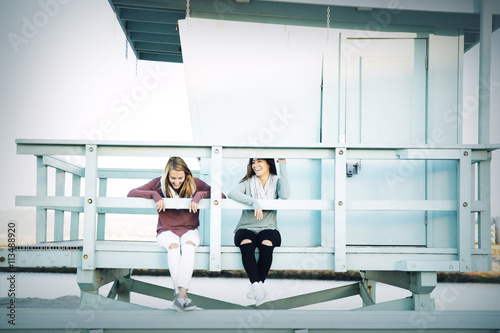 Happy female friends sitting on lifeguard hut at beach photo