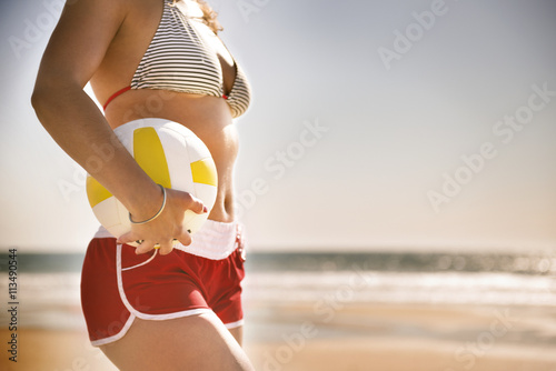 Midsection of young woman holding volleyball on beach against clear sky photo