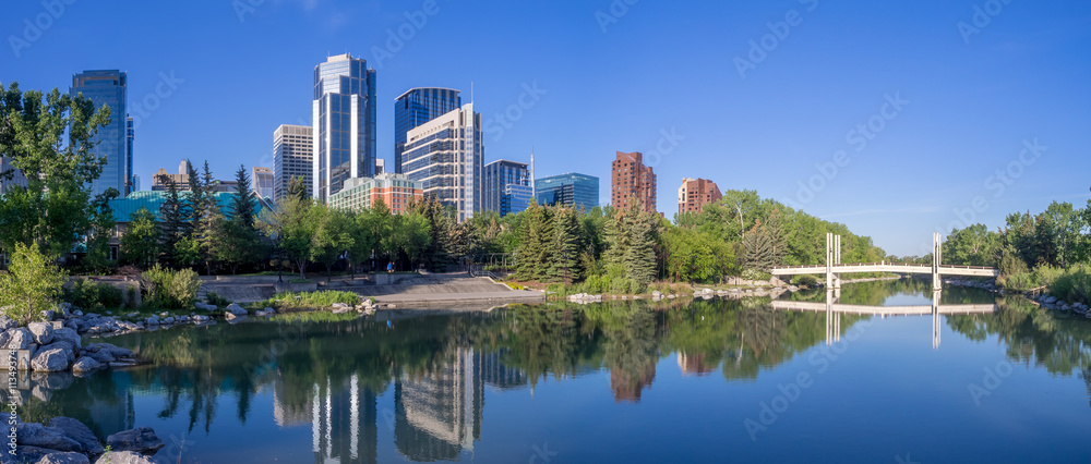 Foot bridge reflected in the Bow River at princes island park and the urban skyline in Calgary Alberta.