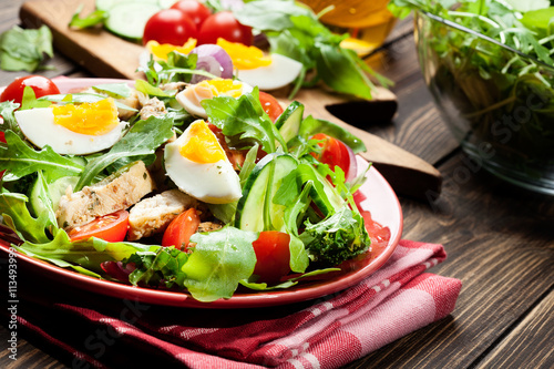Fresh salad with chicken, tomatoes, eggs and arugula on plate