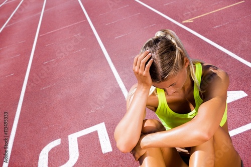 Sporty woman sitting down and feeling disappointed  against race track